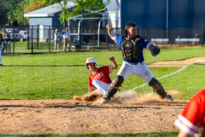 A Smyrna player slides into home as Dover's catcher Ryan Perkins prepares to throw to first.