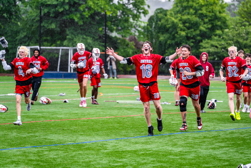 Photo Gallery: 2026 DIAA Boys Lacrosse Quarterfinals, Smyrna vs Wilmington Friends 1 Supinski (18), senior Timothy Pepeta (20), junior Christopher Nacrelli (4) and sophomore Alec Elwood (32) celebrate the win as rain comes down as it did during the game.